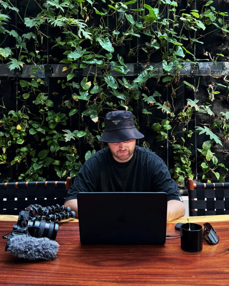Man with laptop in outdoor café, surrounded by plants, embodying remote work lifestyle in Mexico.